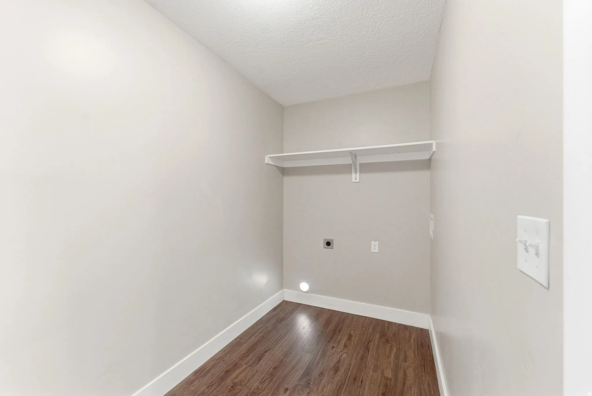 Dedicated utility space off the garage featuring wood-finish flooring, light neutral walls, white baseboards, and a built-in storage shelf