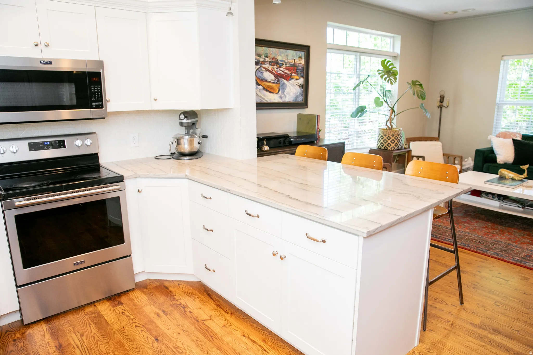 Kitchen featuring a central island with countertop seating, white shaker cabinetry, stainless steel appliances, and wood-finish flooring