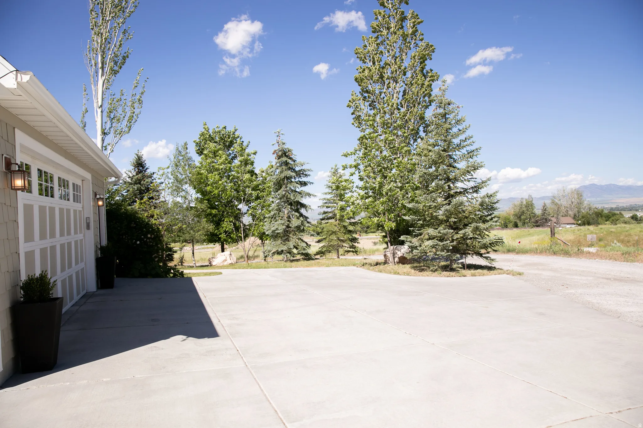 Spacious concrete driveway featuring a two-car garage with carriage-style doors and exterior sconce lighting