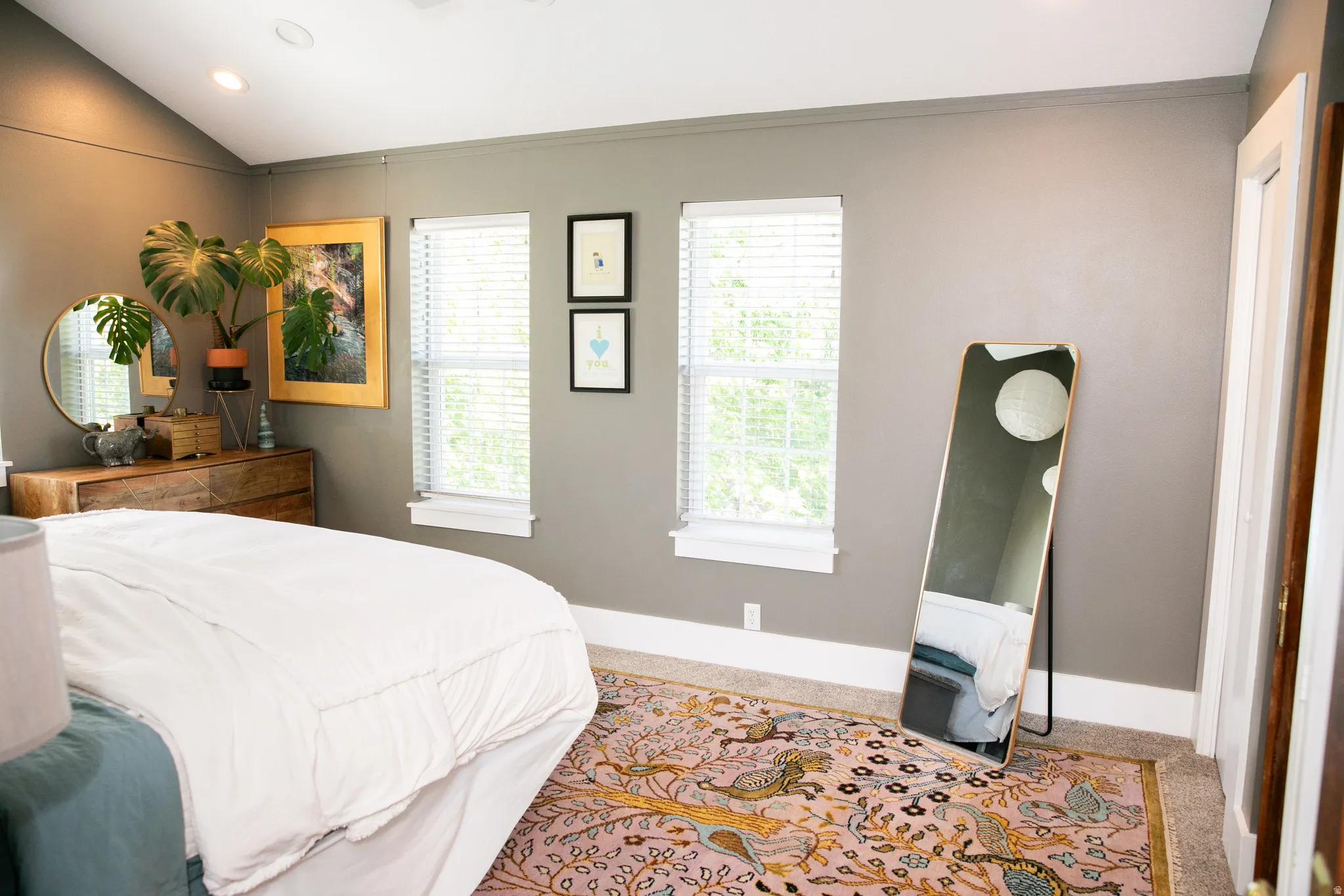 Spacious room featuring vaulted ceilings, recessed lighting, two windows with blinds, a built-in wooden dresser, and a vibrant patterned area rug