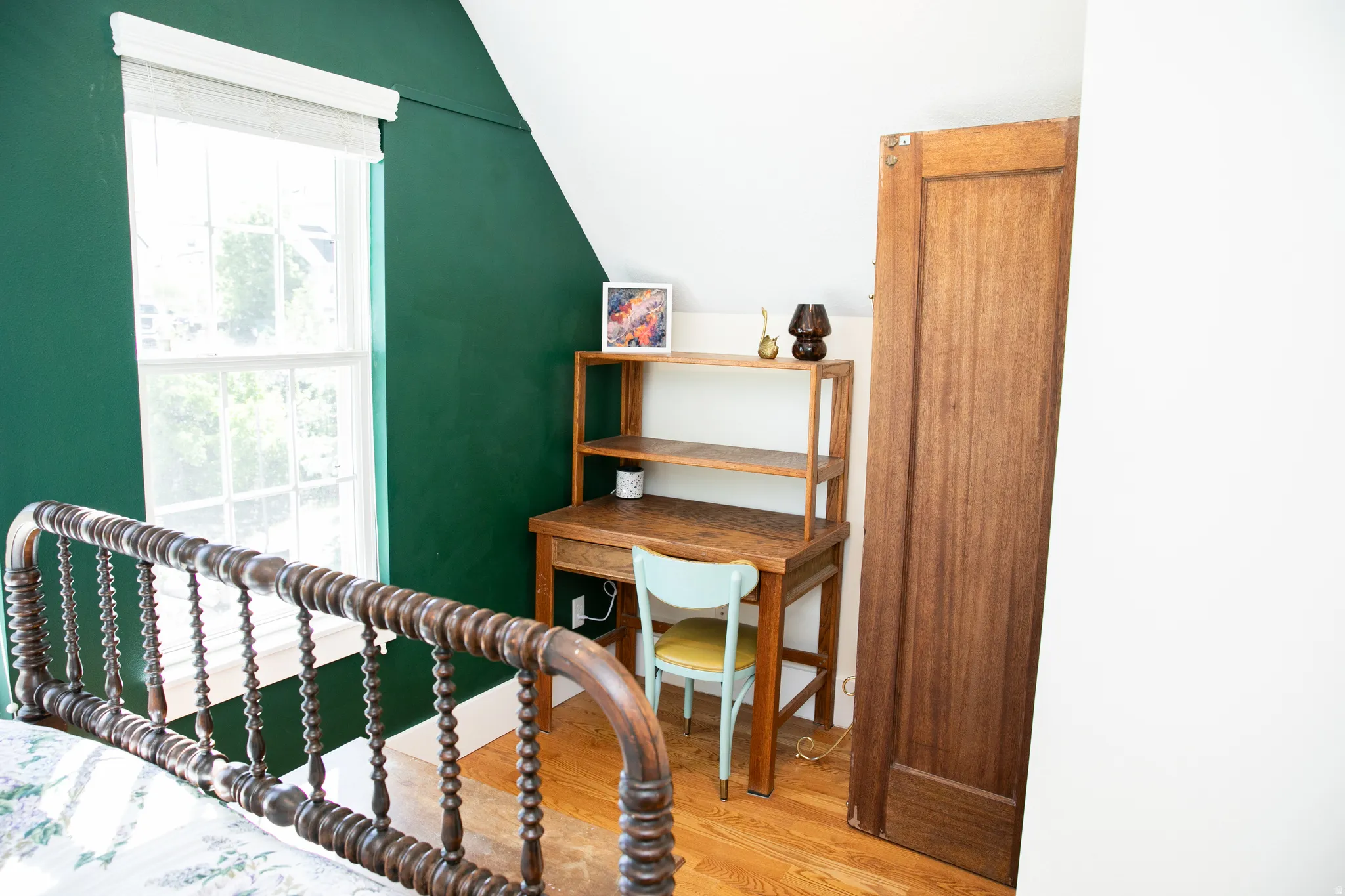 Room with a distinctive emerald green accent wall, hardwood flooring, and a double-hung window with a white frame