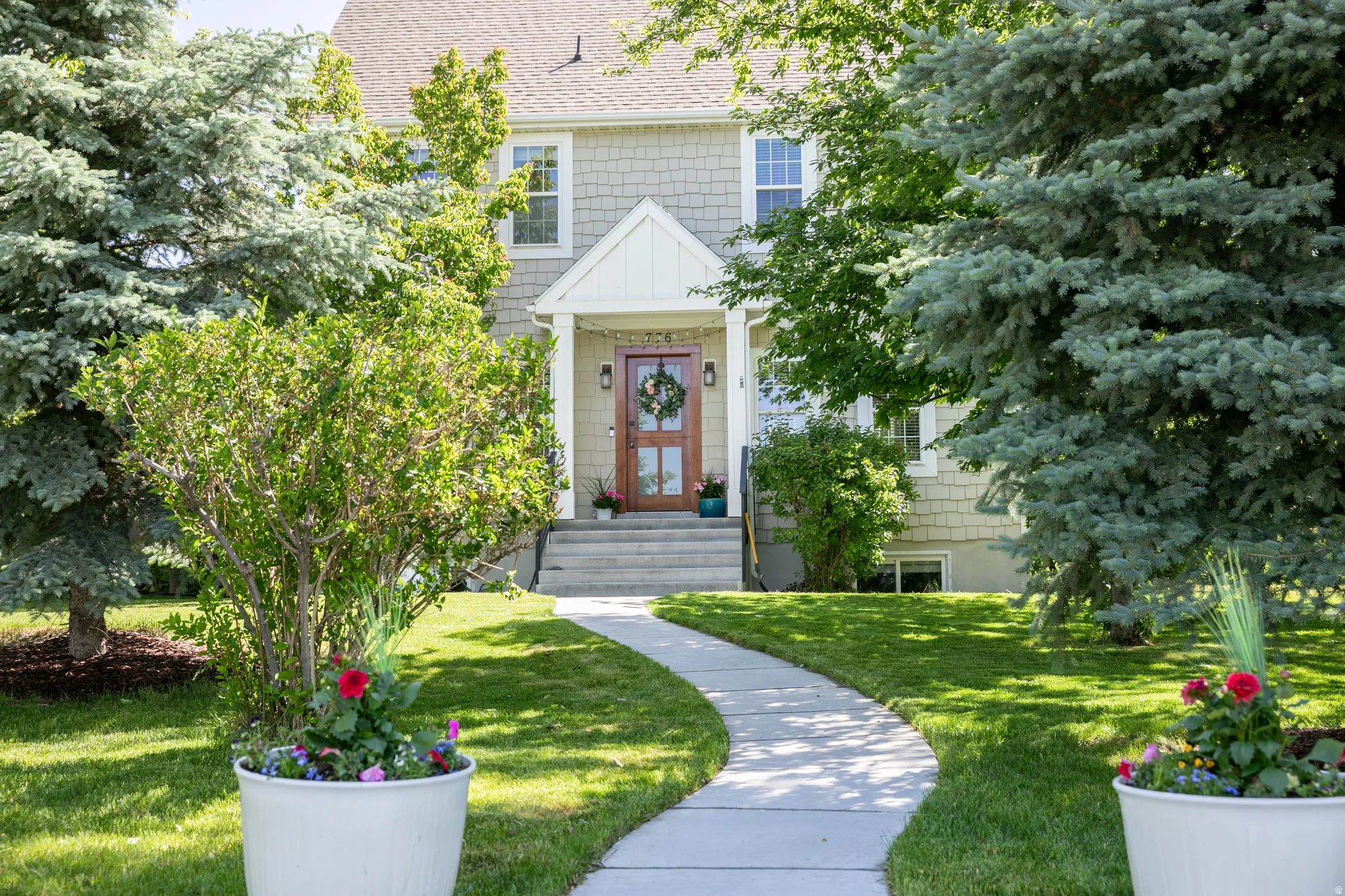 Inviting front exterior featuring a curved concrete pathway, mature evergreen trees, and manicured lawn