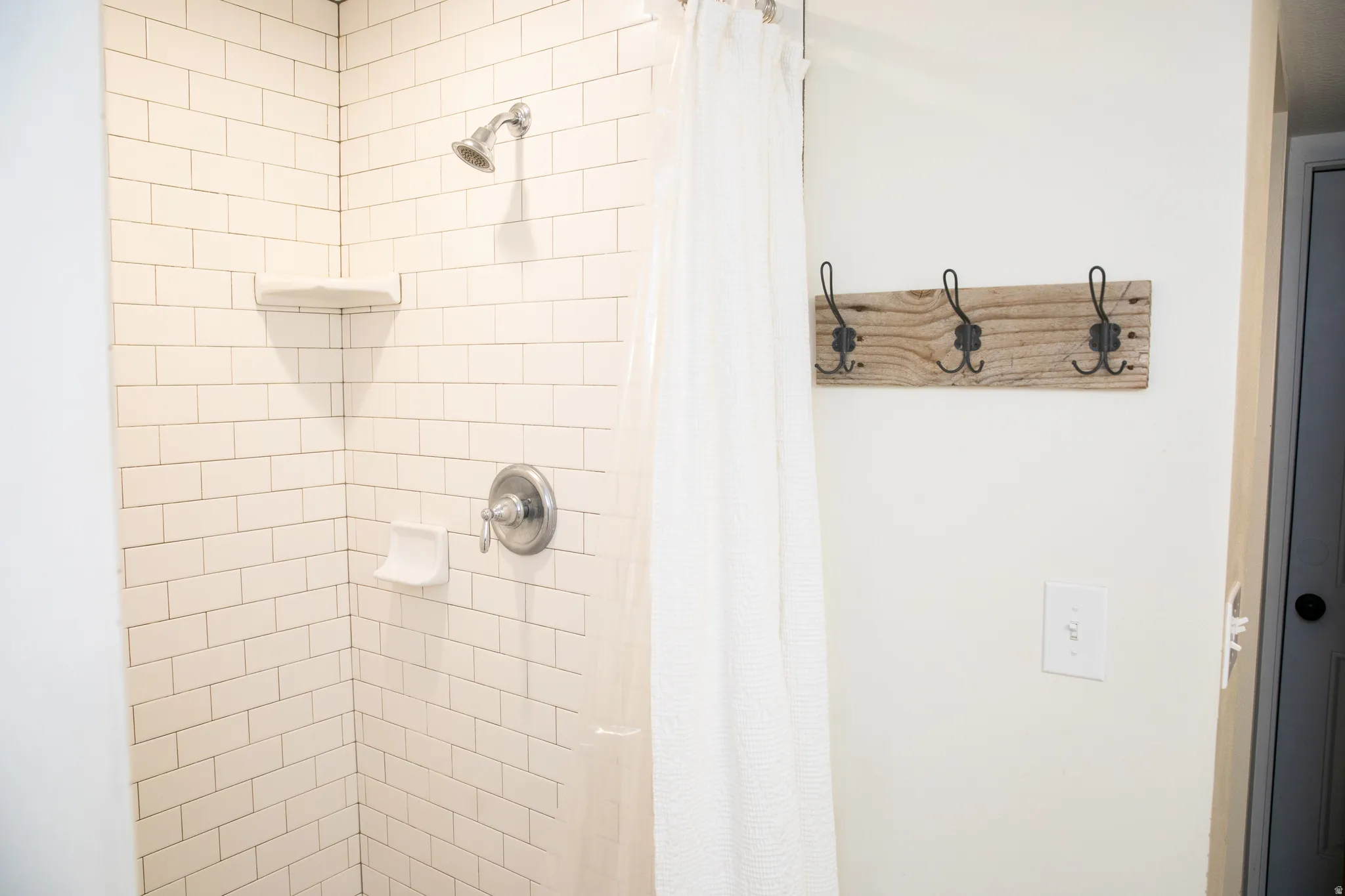 Shower stall featuring white subway tile, a built-in corner shelf, and a chrome shower head and controls
