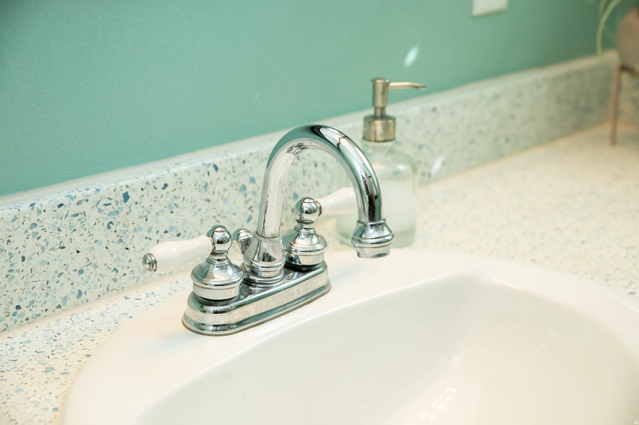 White vanity sink with a chrome two-handle faucet and integrated terrazzo-style countertop