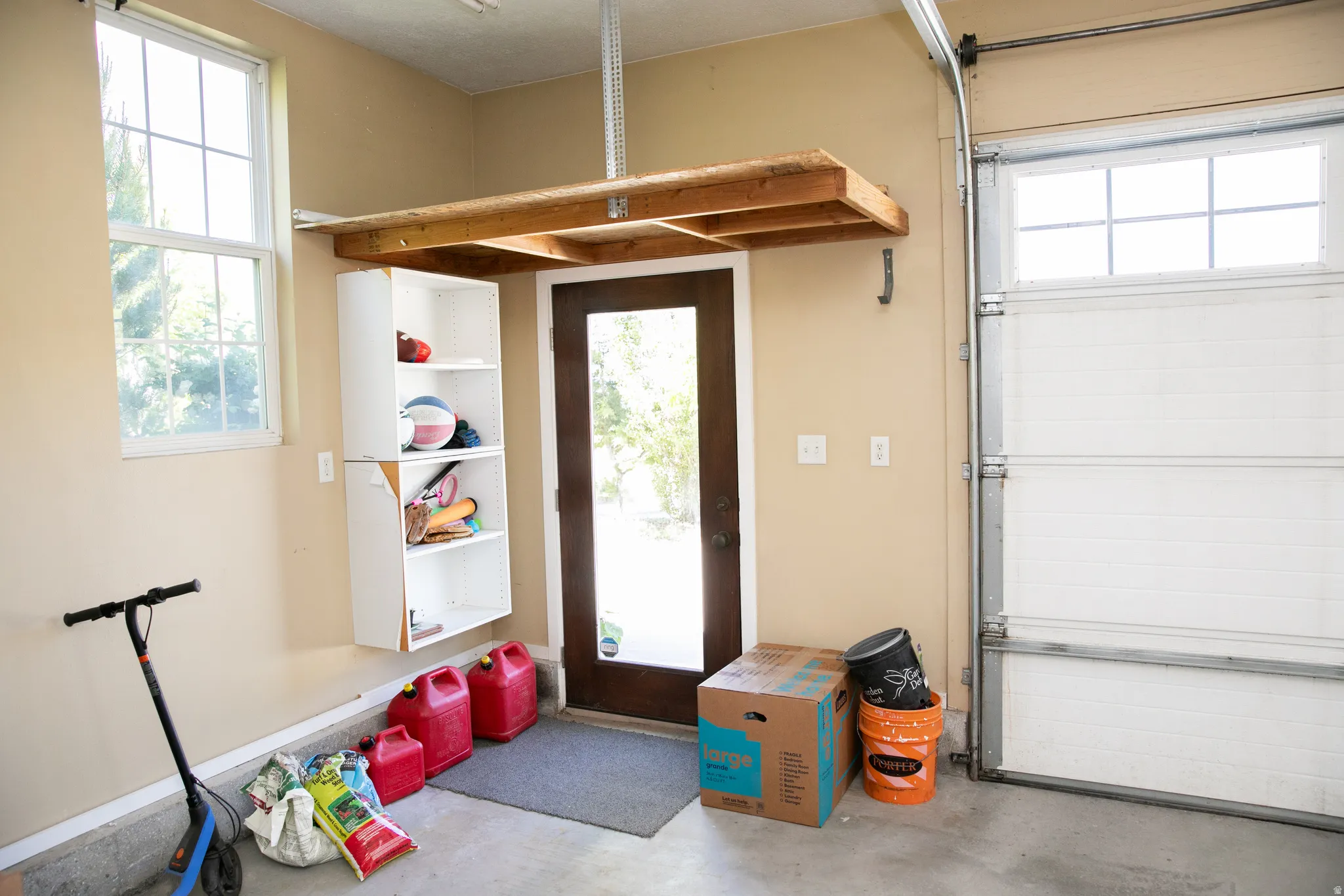 Garage space featuring an overhead storage shelf, built-in shelving, a full-lite exterior door, and a garage door with upper window panes