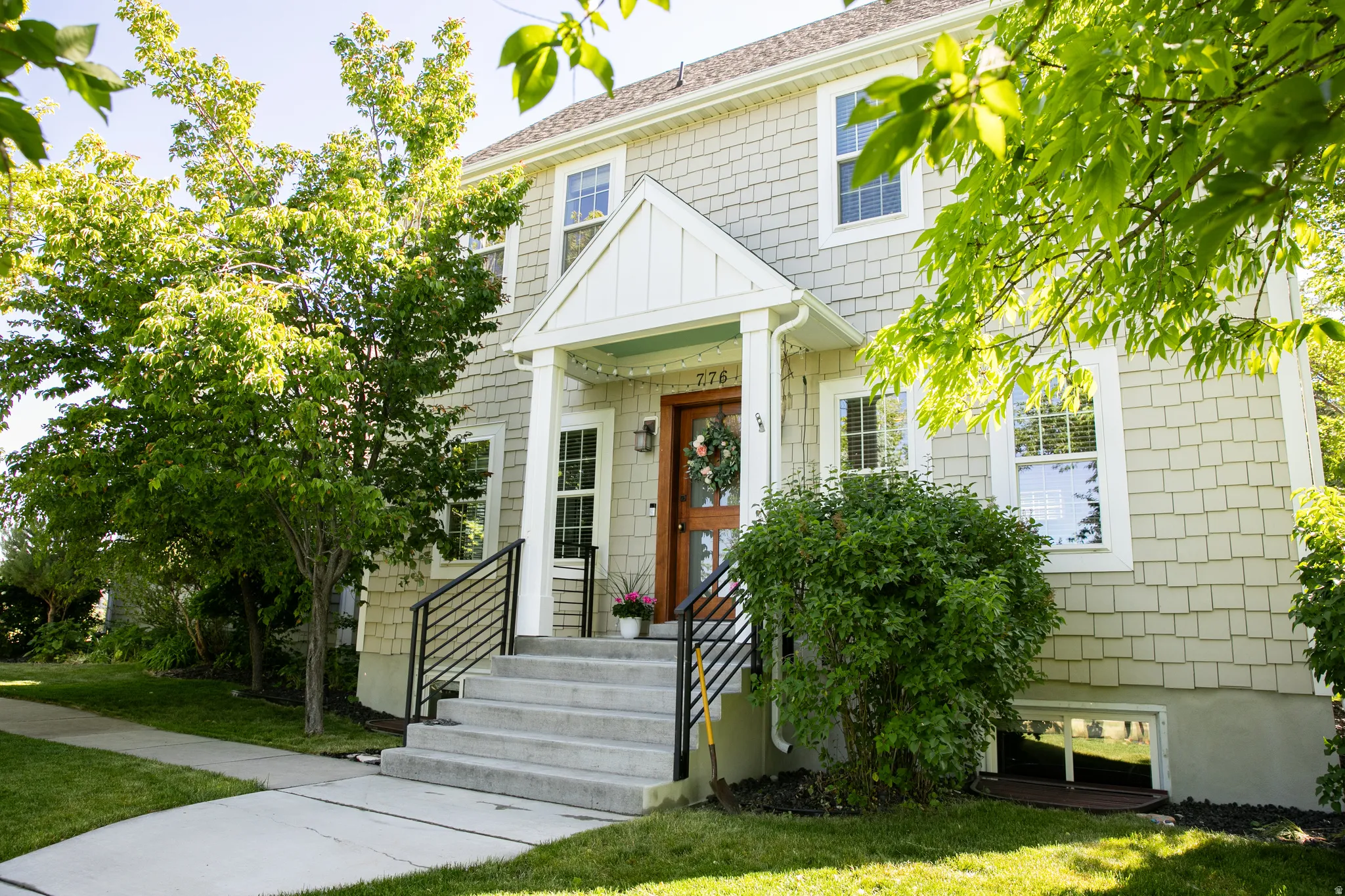 Exterior featuring shingle siding, a covered entry porch, concrete steps with black metal railings, and a solid wood entry door