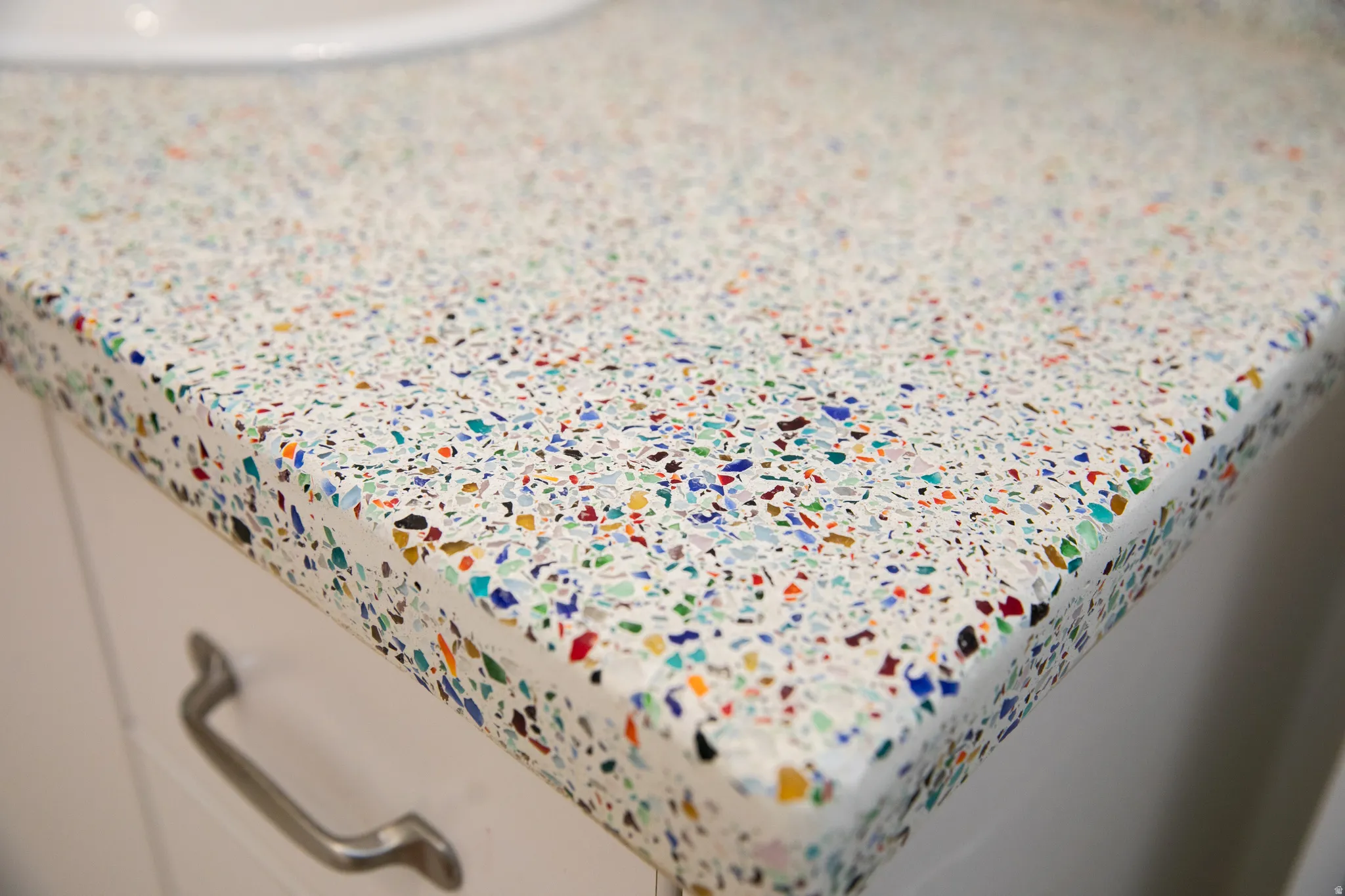 White countertop with colorful aggregate, featuring a rounded edge and a cabinet with a brushed nickel drawer pull
