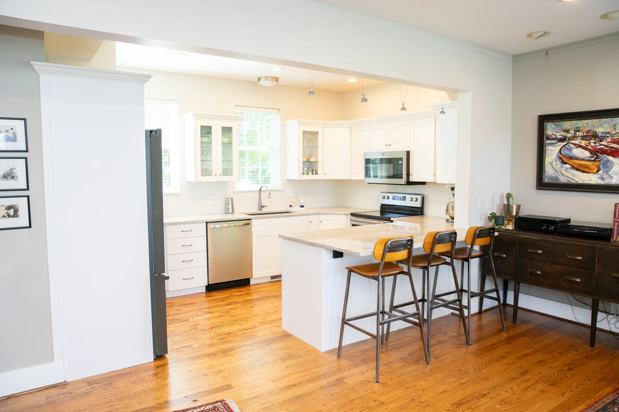 Open-concept kitchen featuring white cabinetry, stainless steel appliances, a breakfast bar island, light-toned countertops, and wood-finish flooring