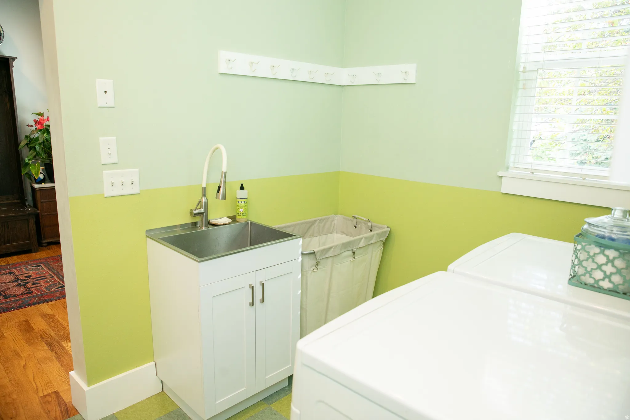 Dedicated utility space featuring a stainless steel sink, white cabinetry, and a wall-mounted coat rack