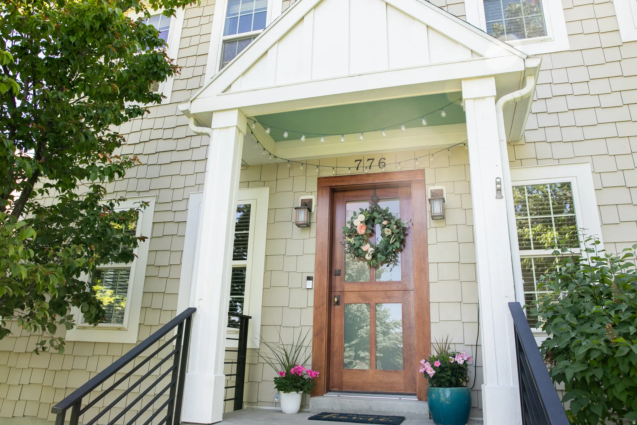 Shingle-sided exterior with a covered entry, featuring a wood-panel front door with glass inserts, white trim windows, and black metal railings