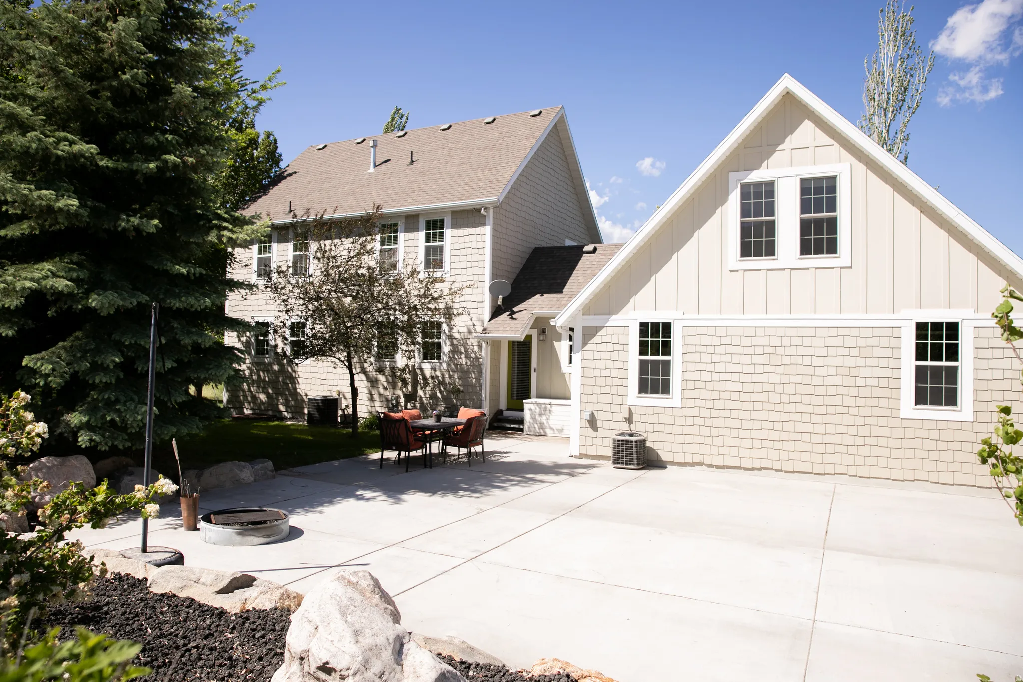 Expansive concrete patio area featuring a built-in fire pit, surrounded by decorative rock landscaping