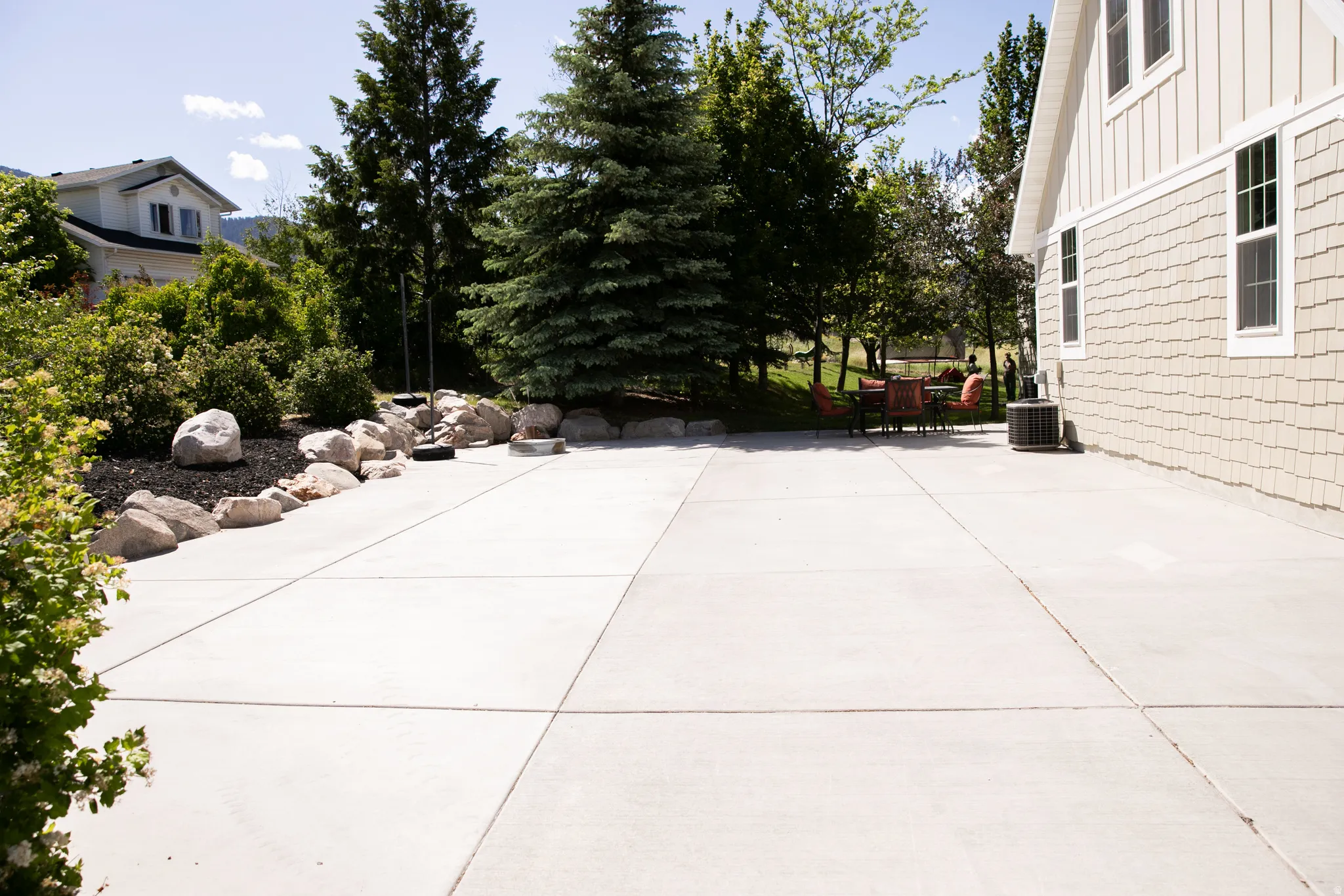 Expansive concrete patio bordered by natural rock landscaping and mature trees