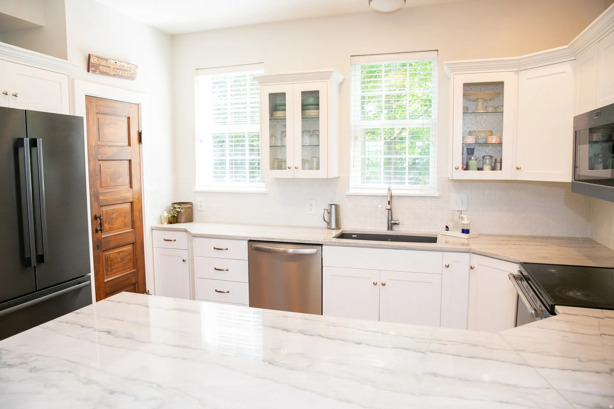 Kitchen featuring a large central island with a stone countertop, white cabinetry with various storage options, stainless steel appliances, and a dark wood-finish paneled door