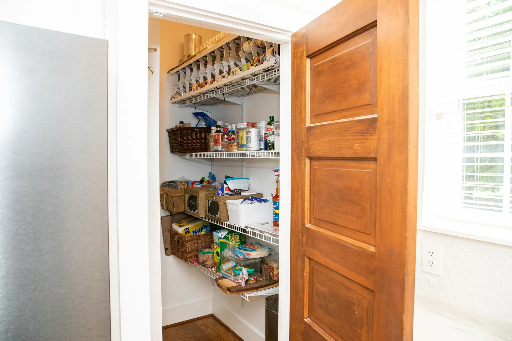 Kitchen pantry featuring multiple wire shelving units, a paneled wood door, and wood-finish flooring