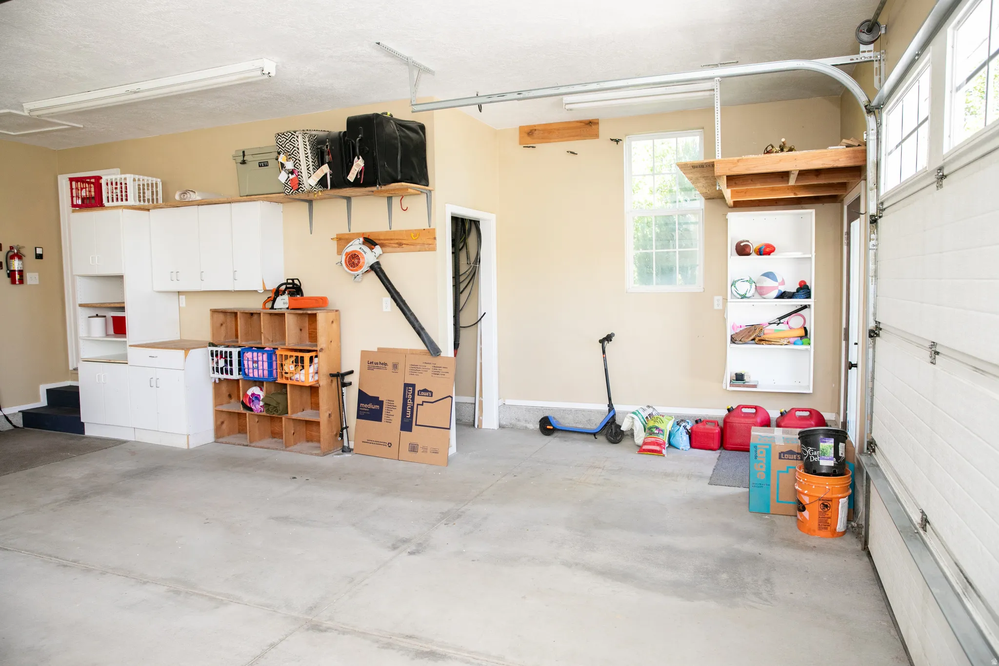 Garage featuring concrete flooring, white built-in cabinetry, an overhead storage shelf, and two windows