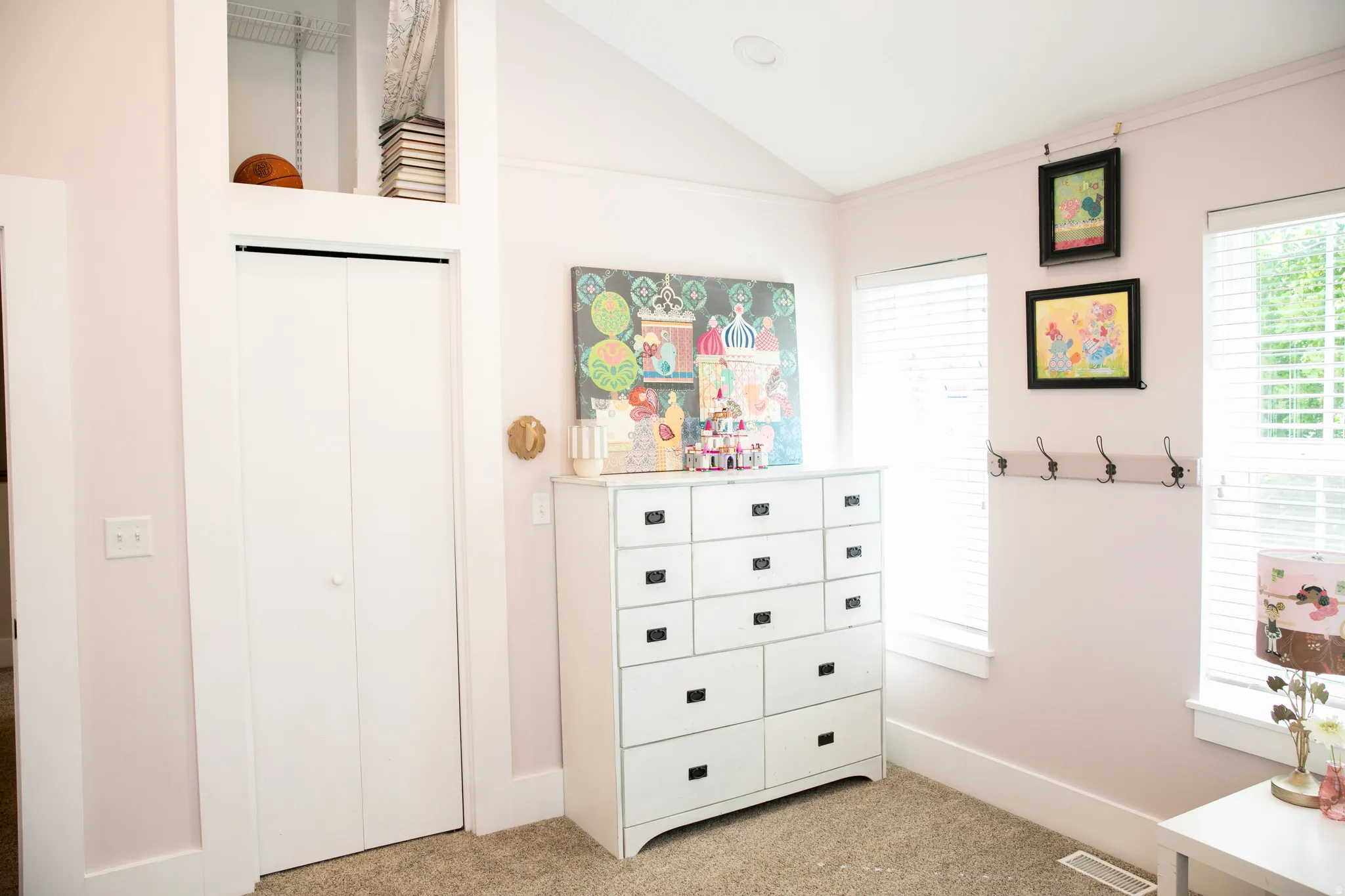 Vaulted ceiling bedroom with neutral carpeting, white bi-fold closet doors, and two windows featuring white blinds