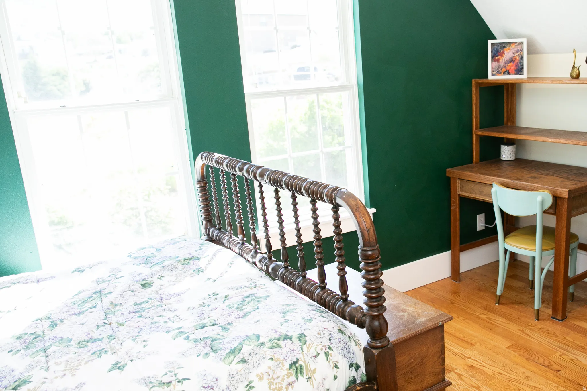 Bright room featuring a wood-finish bed frame, dual sash windows, hardwood flooring, a built-in wood-finish desk with shelving, and green painted walls