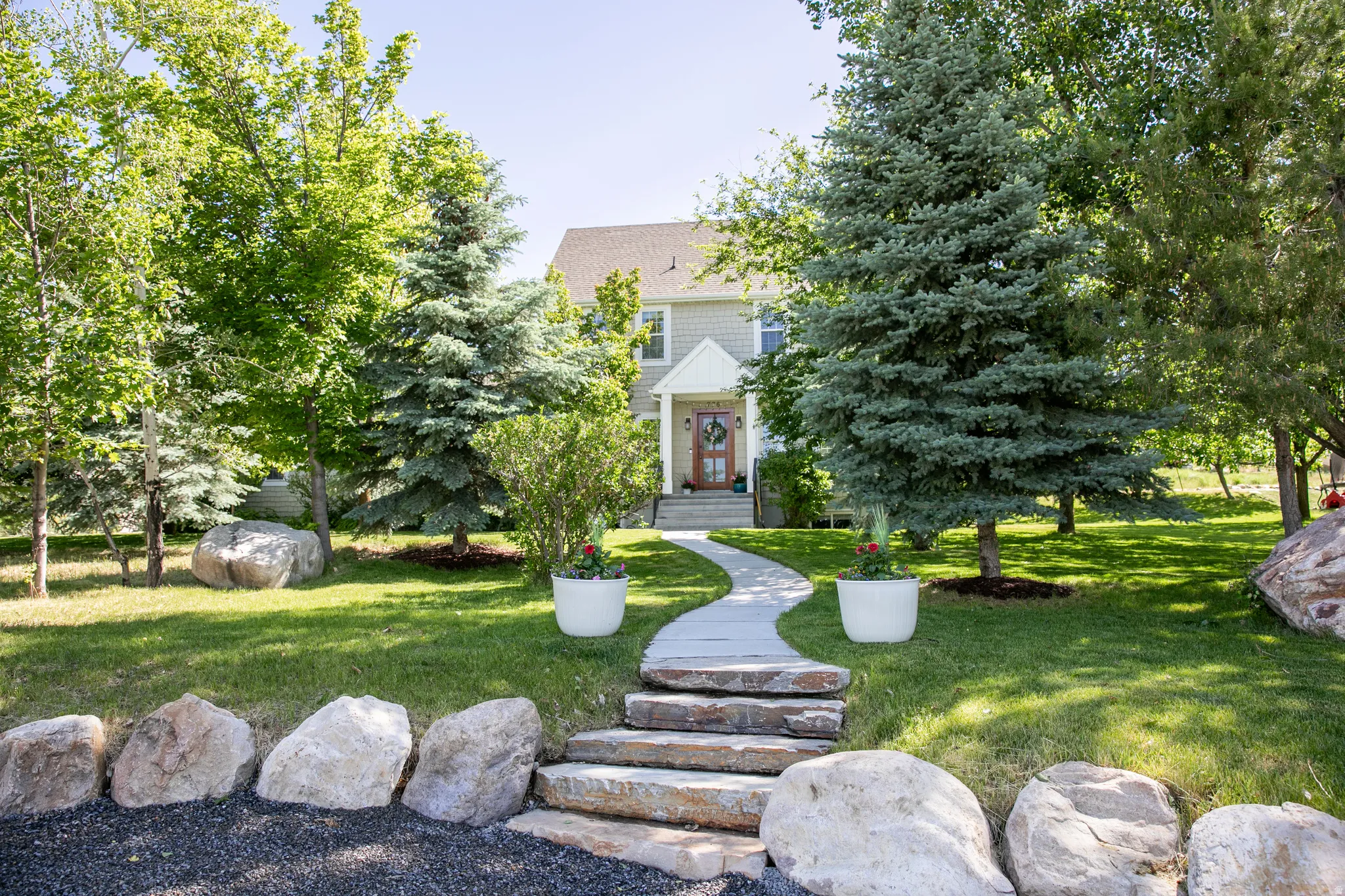 Expansive front yard featuring a winding stone pathway, mature trees, and natural rock landscaping