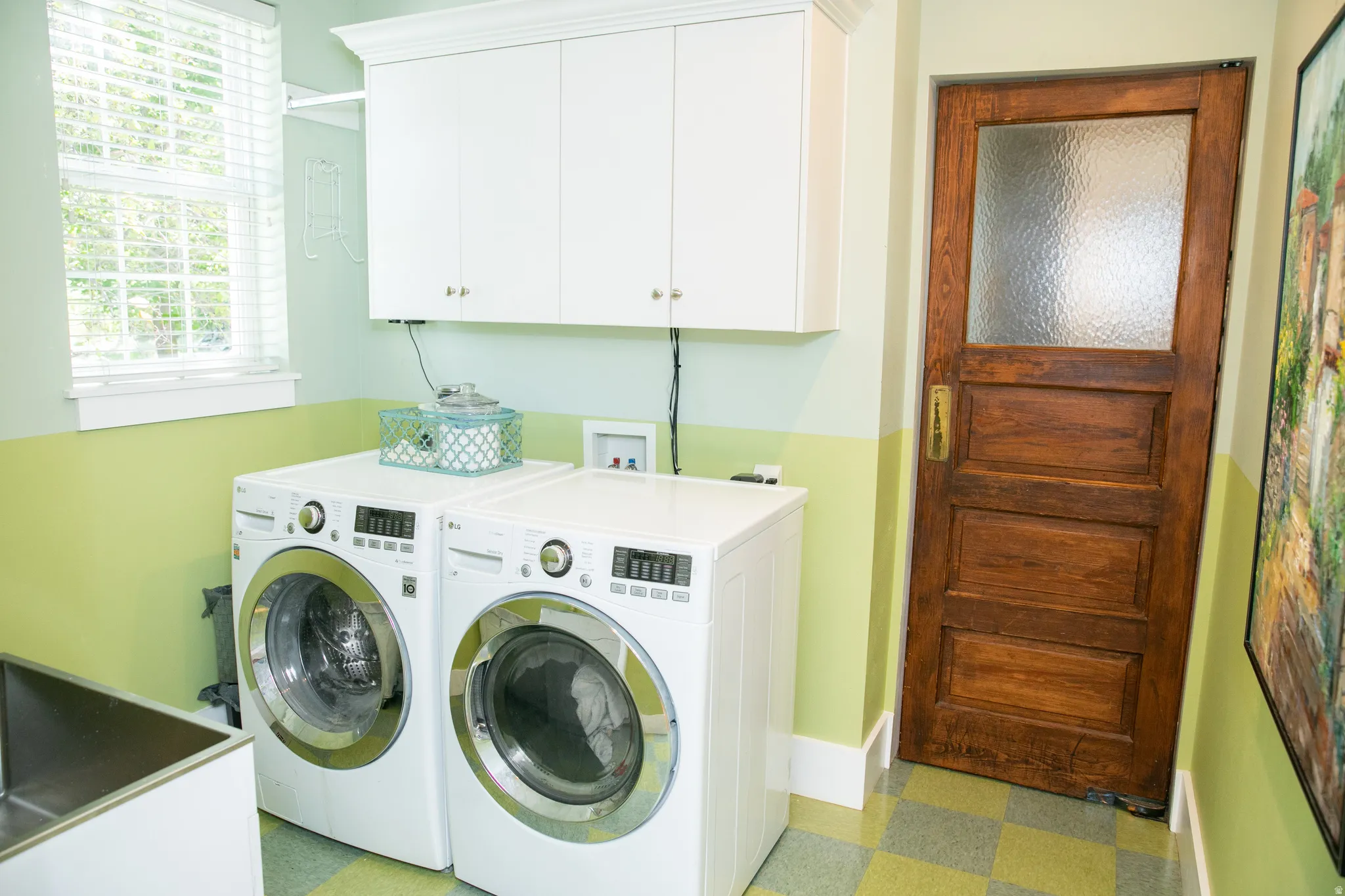 Laundry area featuring white cabinetry, a utility sink, and a wood-panel door with privacy glass