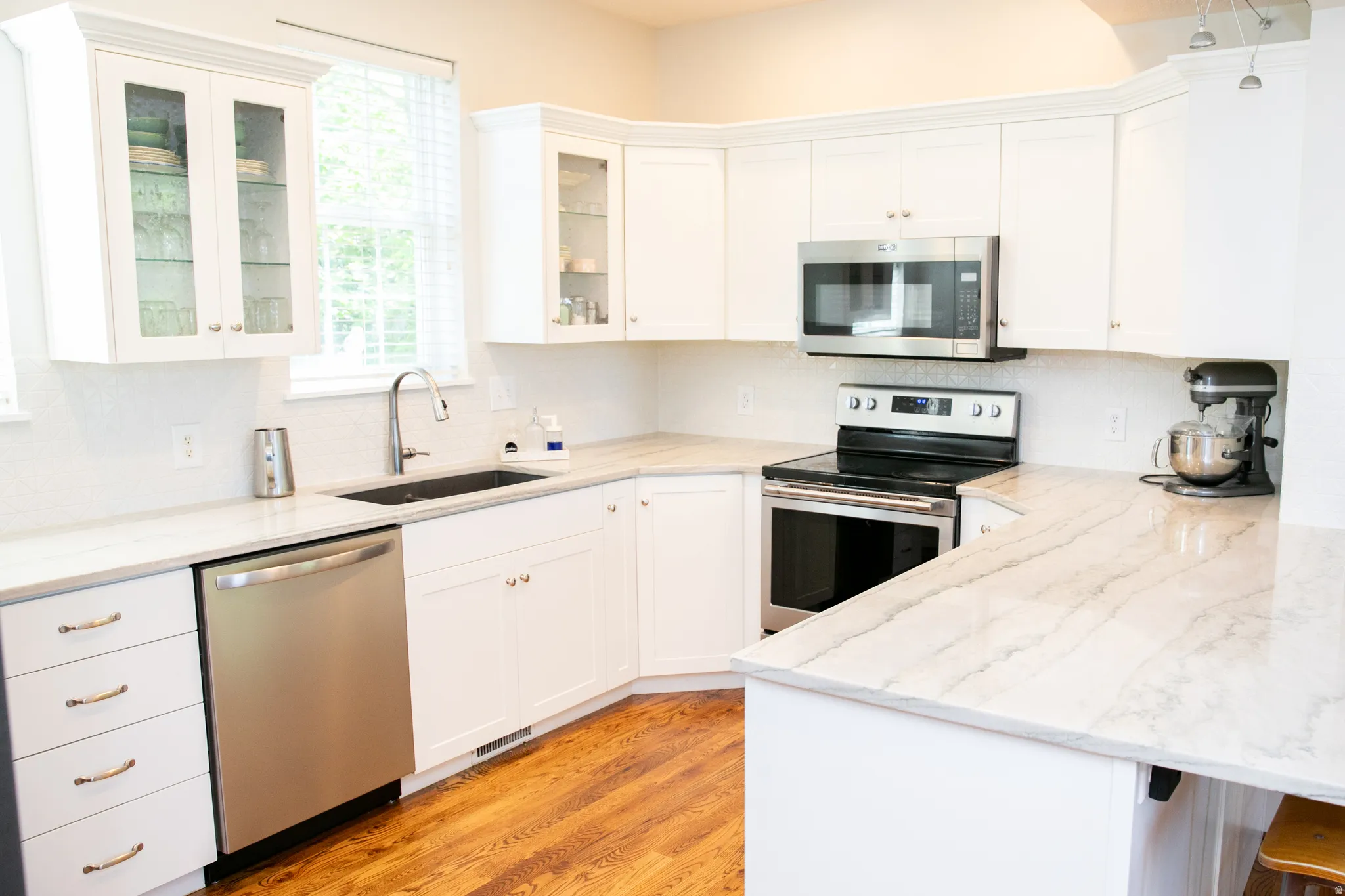 Bright kitchen featuring white cabinetry, stone countertops, stainless steel appliances, a built-in microwave, and wood-finish flooring