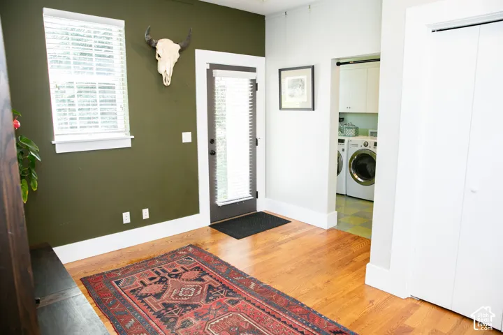 main floor mudroom with rich hardwood flooring throughout, featuring a window with blinds, a dark-framed exterior door, and a dedicated laundry area with built-in cabinetry and tile flooring