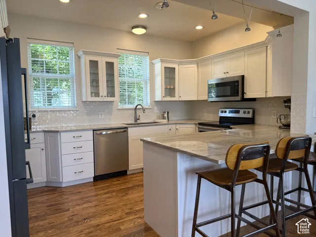 Kitchen featuring a large central island with seating, stainless steel appliances, white shaker cabinetry, patterned tile backsplash, and wood-finish flooring
