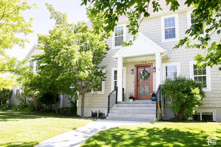 Shingle-sided exterior featuring a covered porch entry, a paneled wood front door with sidelights, and a concrete pathway