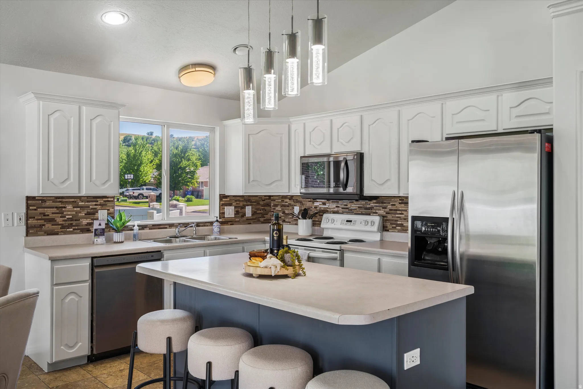 Kitchen featuring white cabinetry, stainless steel appliances, a multi-tone tile backsplash, and a central island with a light-colored countertop