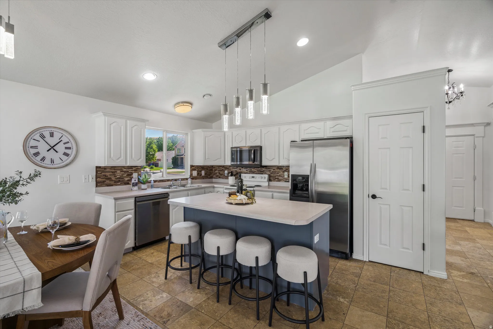 Kitchen featuring white cabinetry, stainless steel appliances, a multi-tone backsplash, and a central island with bar seating