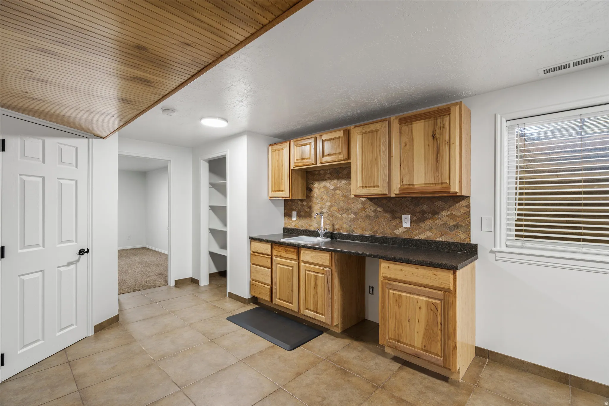 Kitchenette with wood cabinetry, dark countertops, and a mosaic tile backsplash