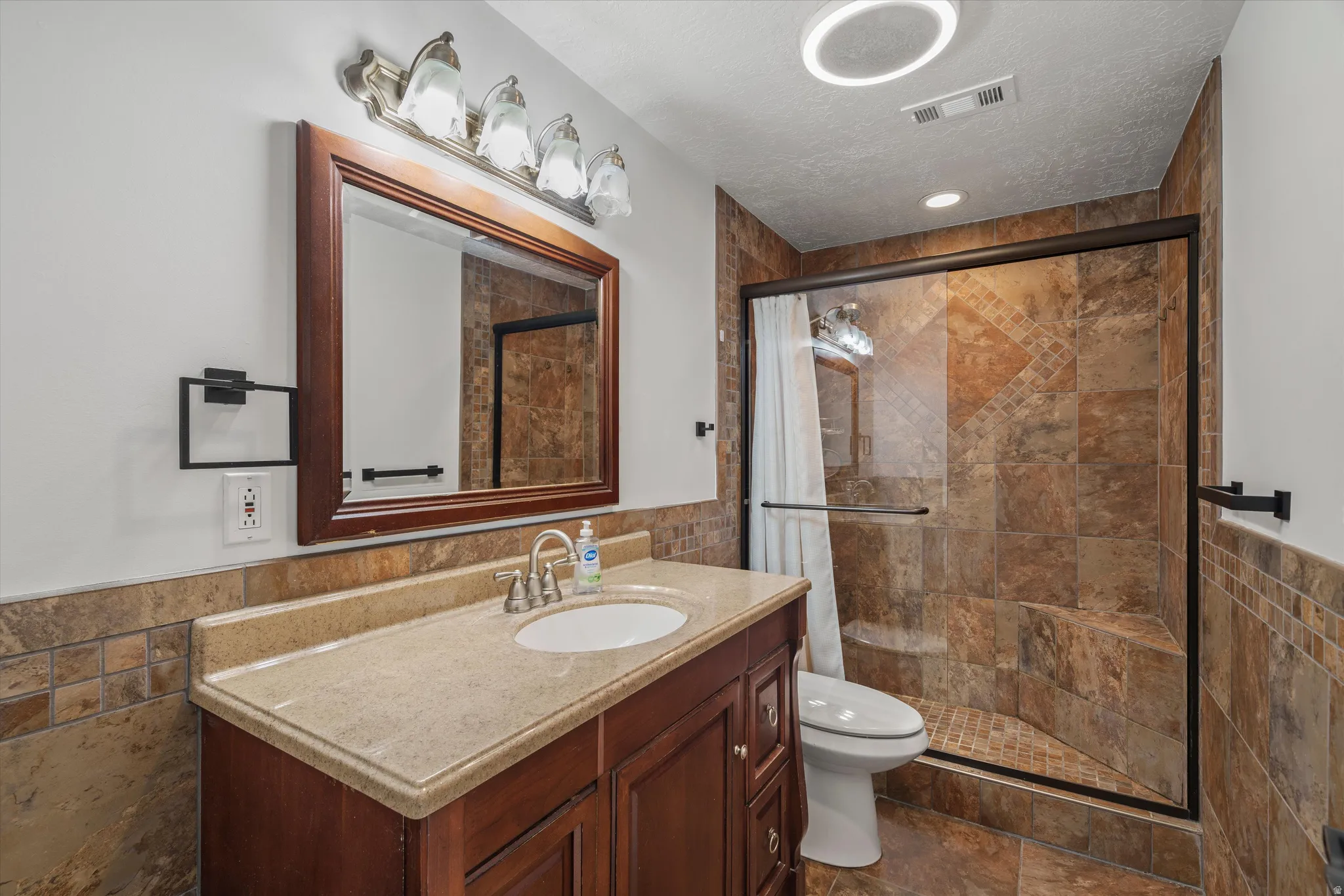 Bathroom featuring a glass-enclosed shower with full tile surround, a built-in shower bench, and a dark wood vanity with an integrated sink and light-toned countertop