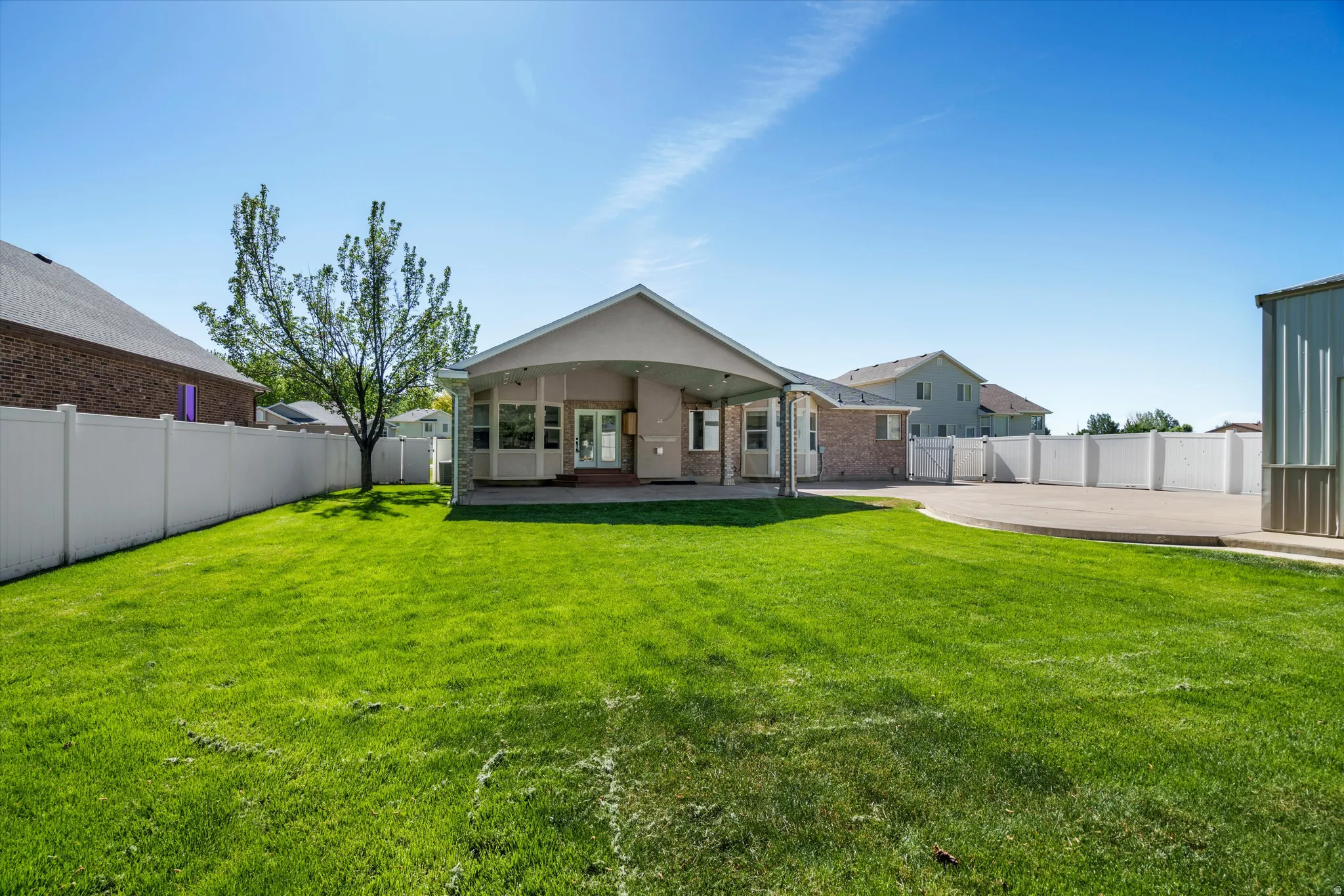 Expansive green lawn with a covered patio, rear entry, full vinyl fencing, mature tree, and a large paved area