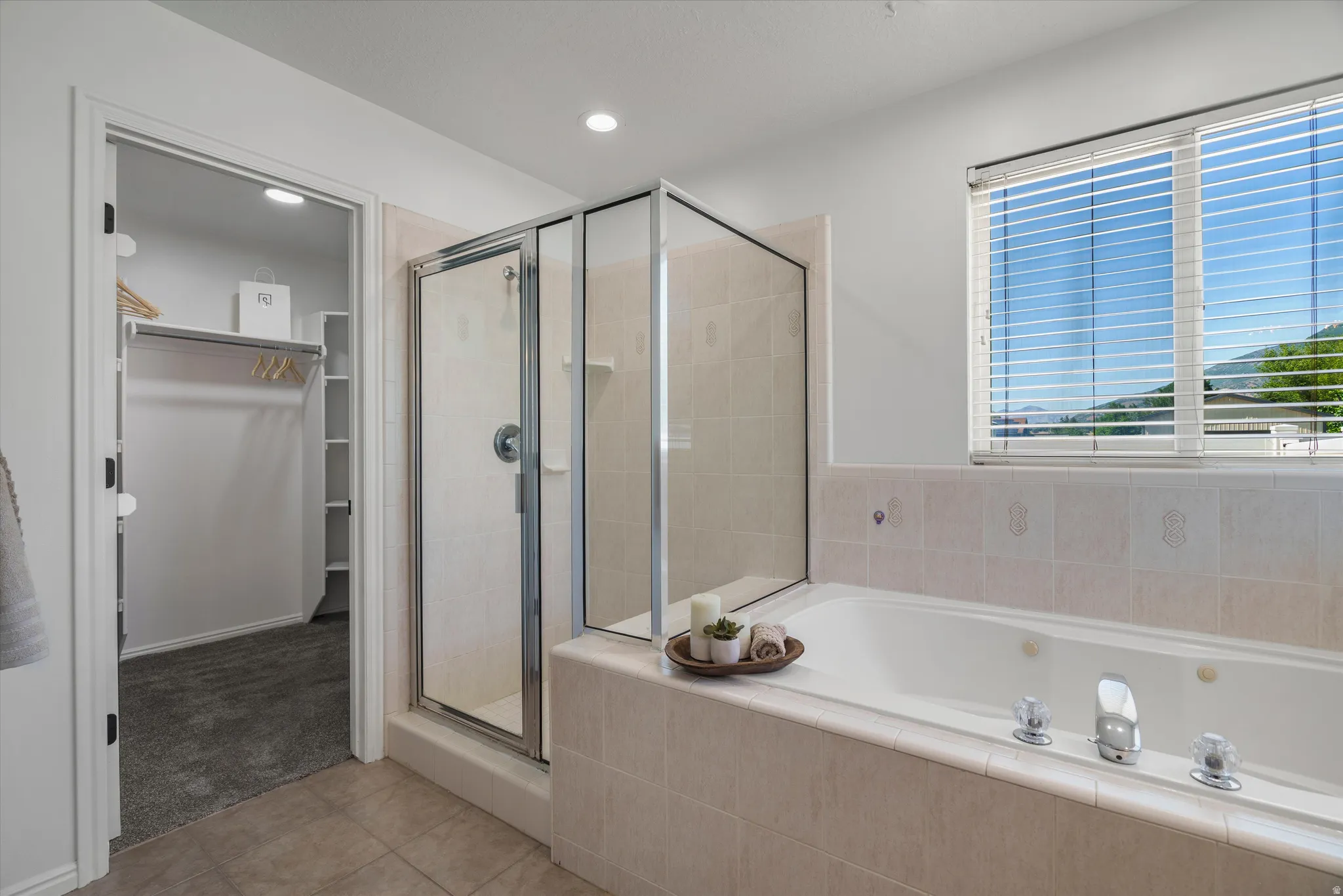 Primary bathroom featuring a built-in jetted tub, a glass-enclosed shower, and a window with horizontal blinds