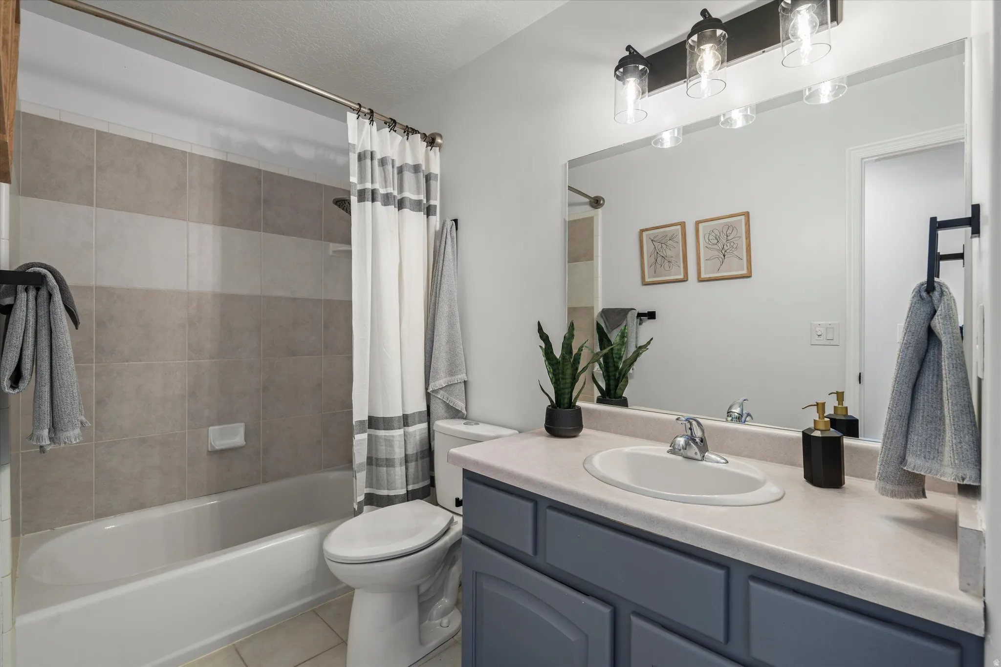 Bathroom featuring a tiled tub-shower combination, a vanity with a light-colored countertop, and a large mirror with a three-light fixture