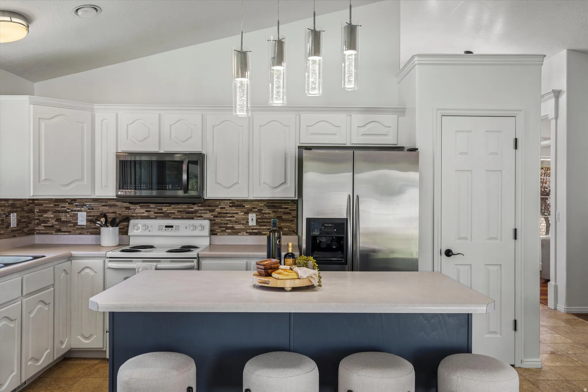 Kitchen featuring vaulted ceilings, white cabinetry, a neutral subway tile backsplash, stainless steel appliances, and a central island with a contrasting base