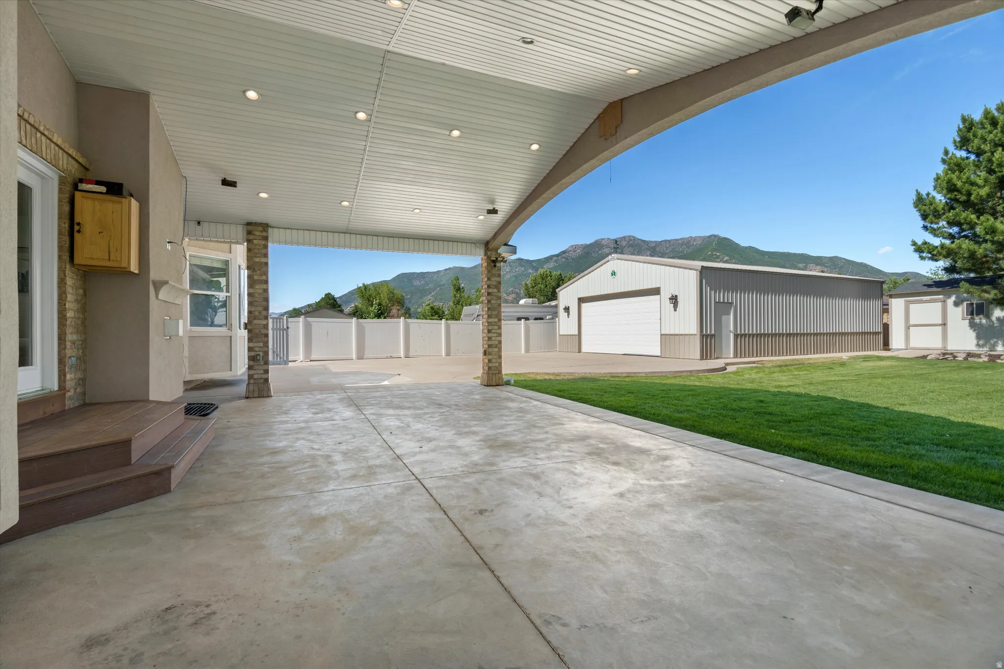 Expansive covered patio featuring recessed lighting, stone-clad columns, and stamped concrete.