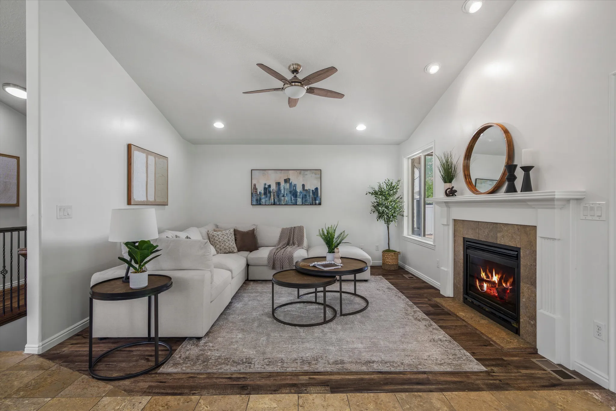 Vaulted ceilings feature recessed lighting and a ceiling fan, complementing the fireplace with a stone surround and white mantel