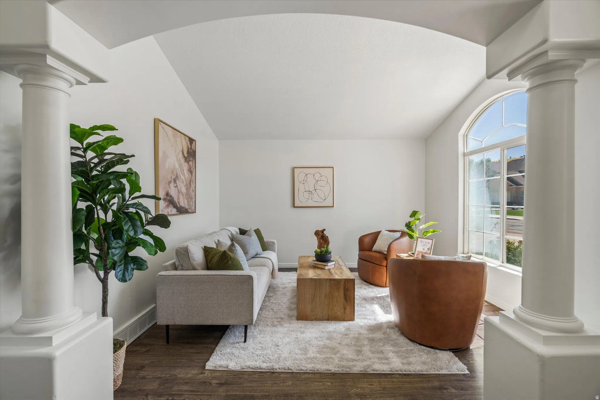 Spacious living area featuring an arched entryway with decorative columns, vaulted ceilings, and wood-finish flooring
