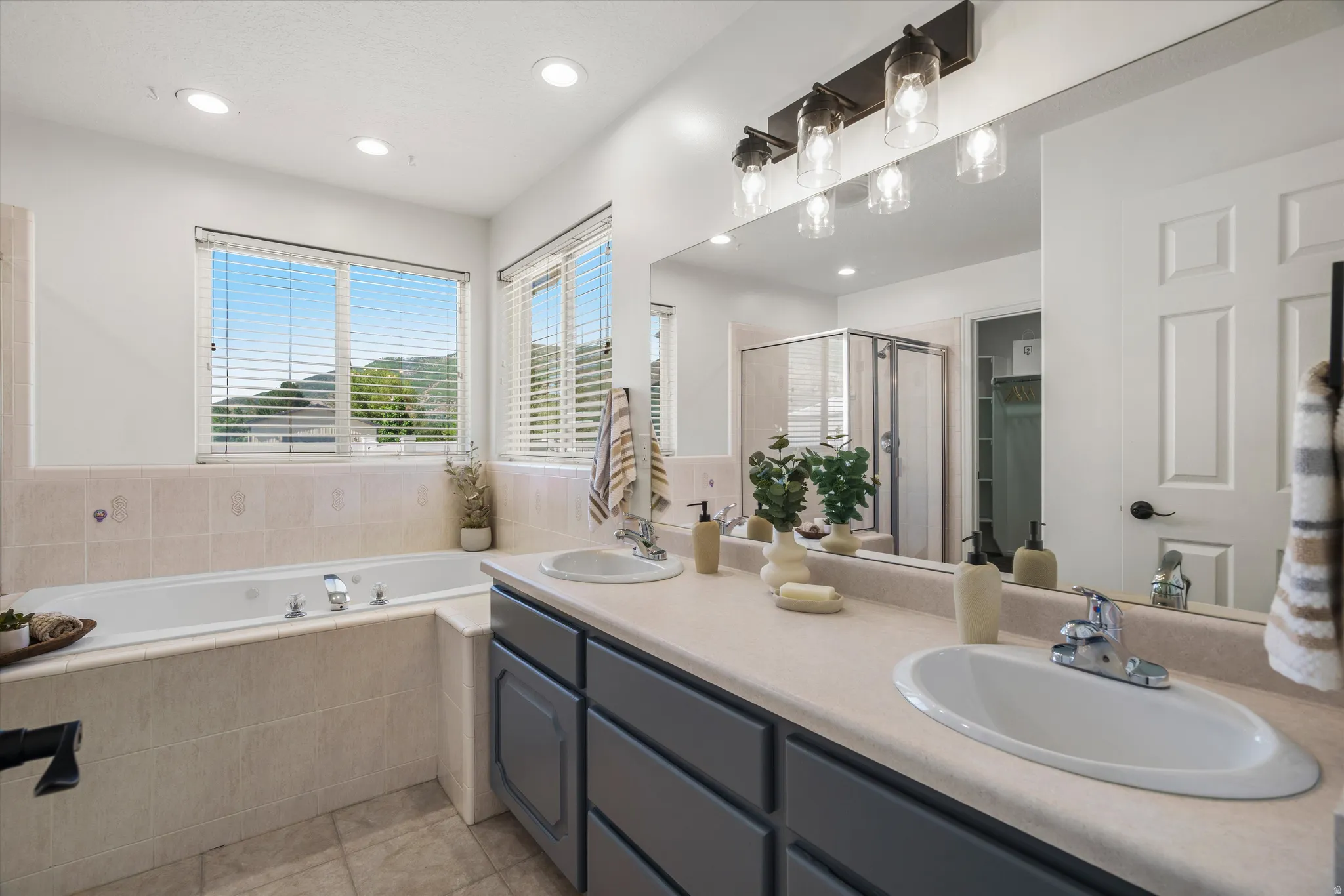 Primary bathroom featuring a built-in tub with surrounding tile, dual vanity with undermount sinks, large mirror, and a glass-enclosed shower