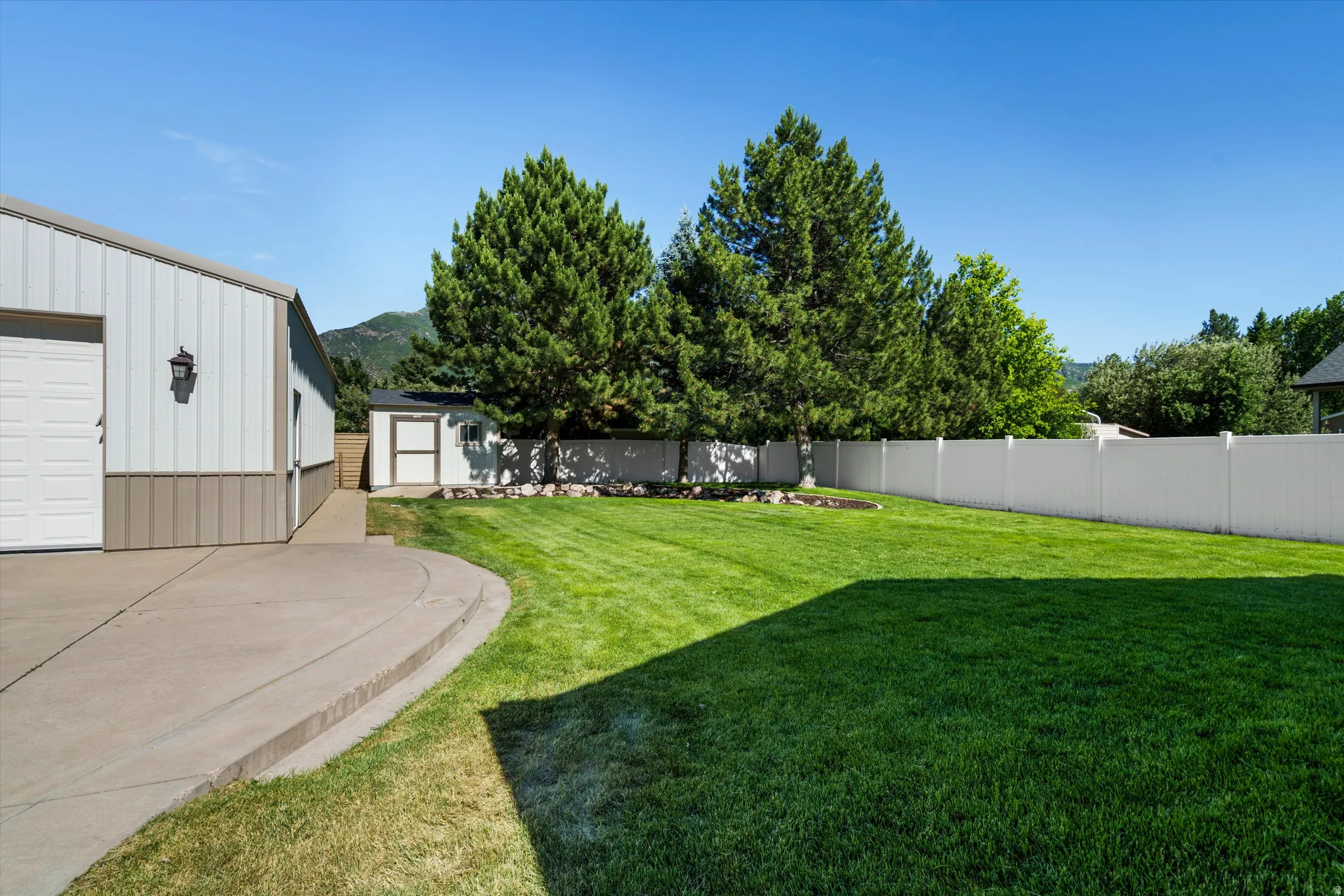 Spacious yard featuring a manicured lawn, an expansive concrete patio, and a white privacy fence