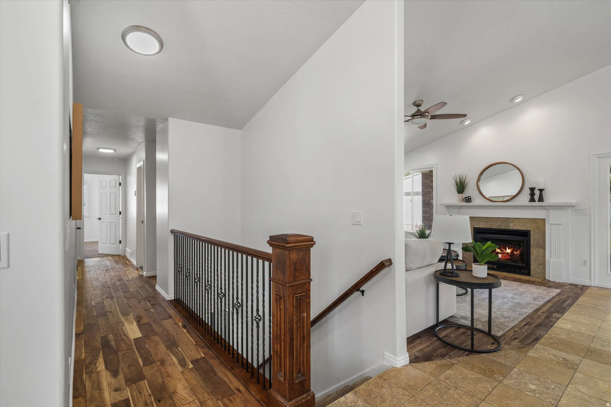 Hardwood flooring throughout the hallway leads to a living space featuring a fireplace with a stone surround and a vaulted ceiling