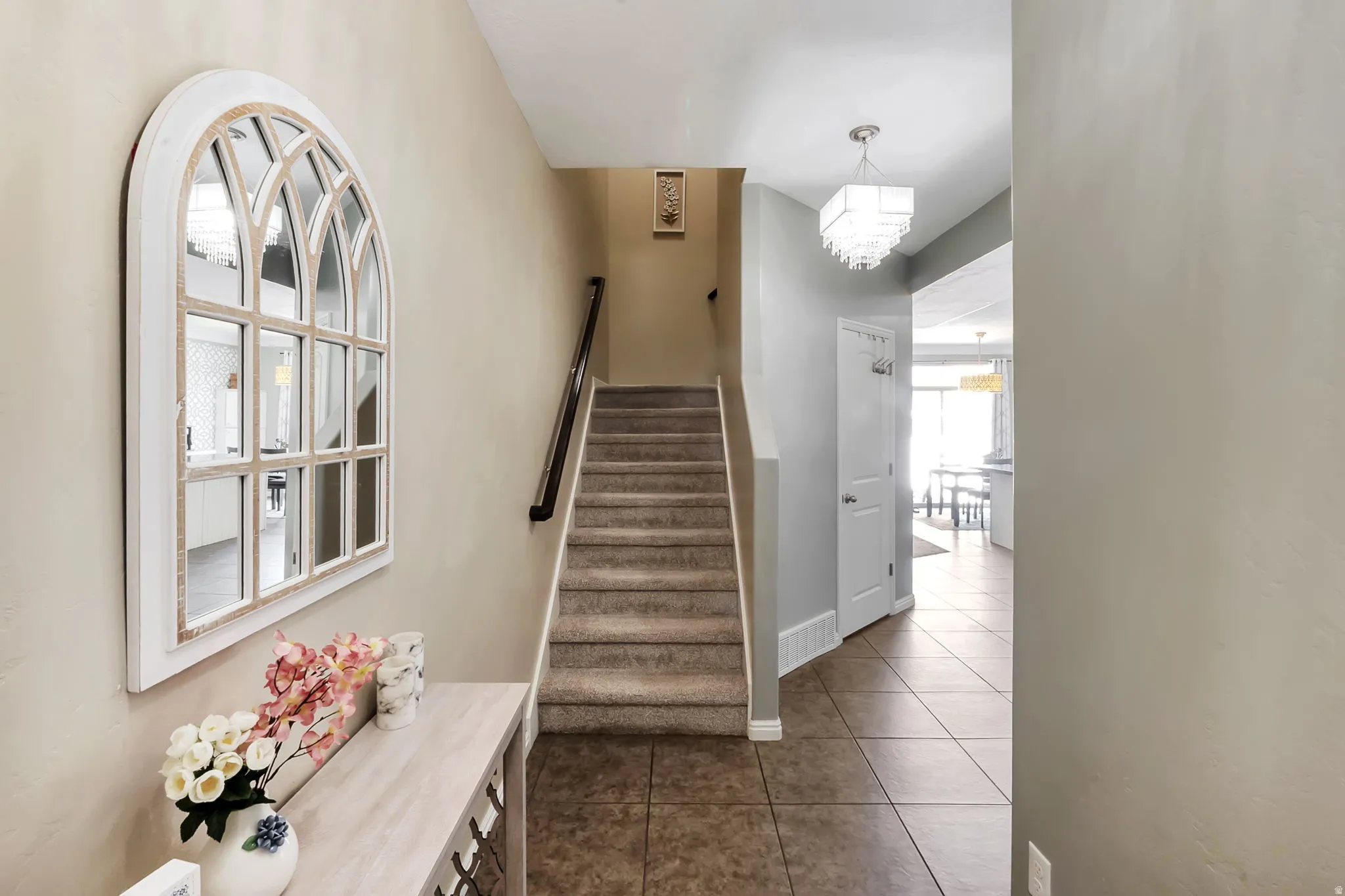 Foyer featuring ceramic tile flooring, carpeted staircase with wood handrail, and a contemporary multi-tiered chandelier