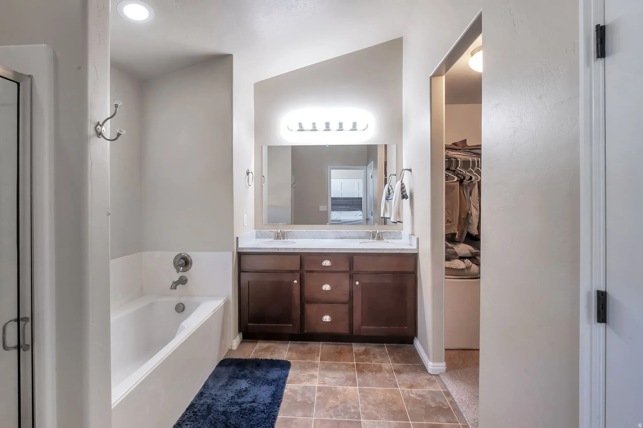 Bathroom featuring a dual vanity with a dark wood-finish cabinet and stone-look countertop, a bathtub with tile surround, and an adjacent walk-in shower with a glass enclosure