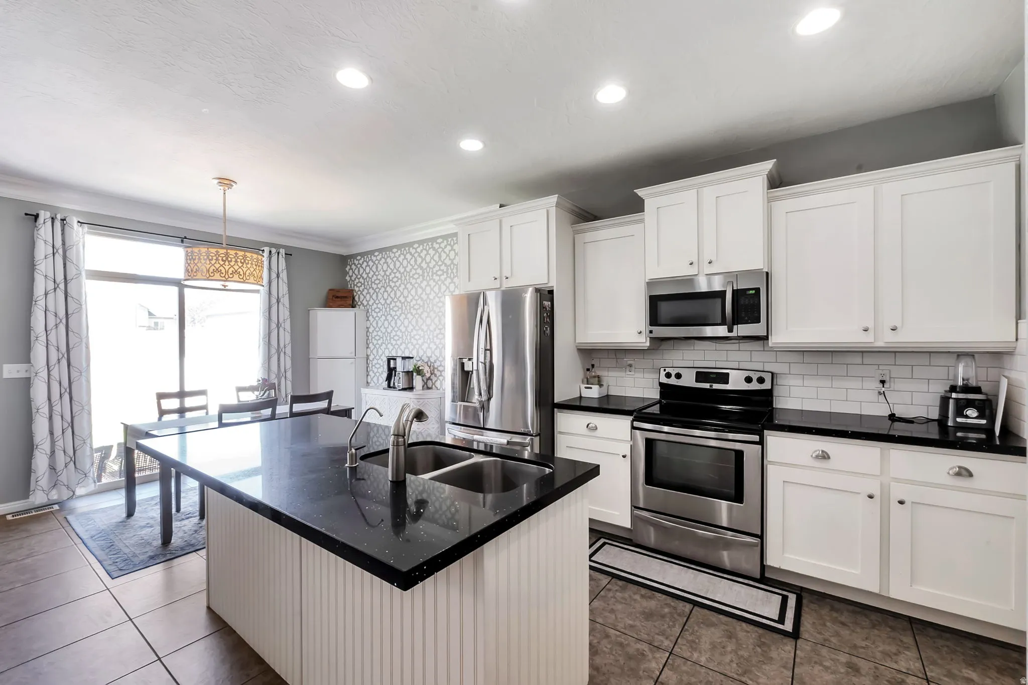 Kitchen featuring a large island with an undermount double sink, white cabinetry, black countertops, stainless steel appliances, and subway tile backsplash