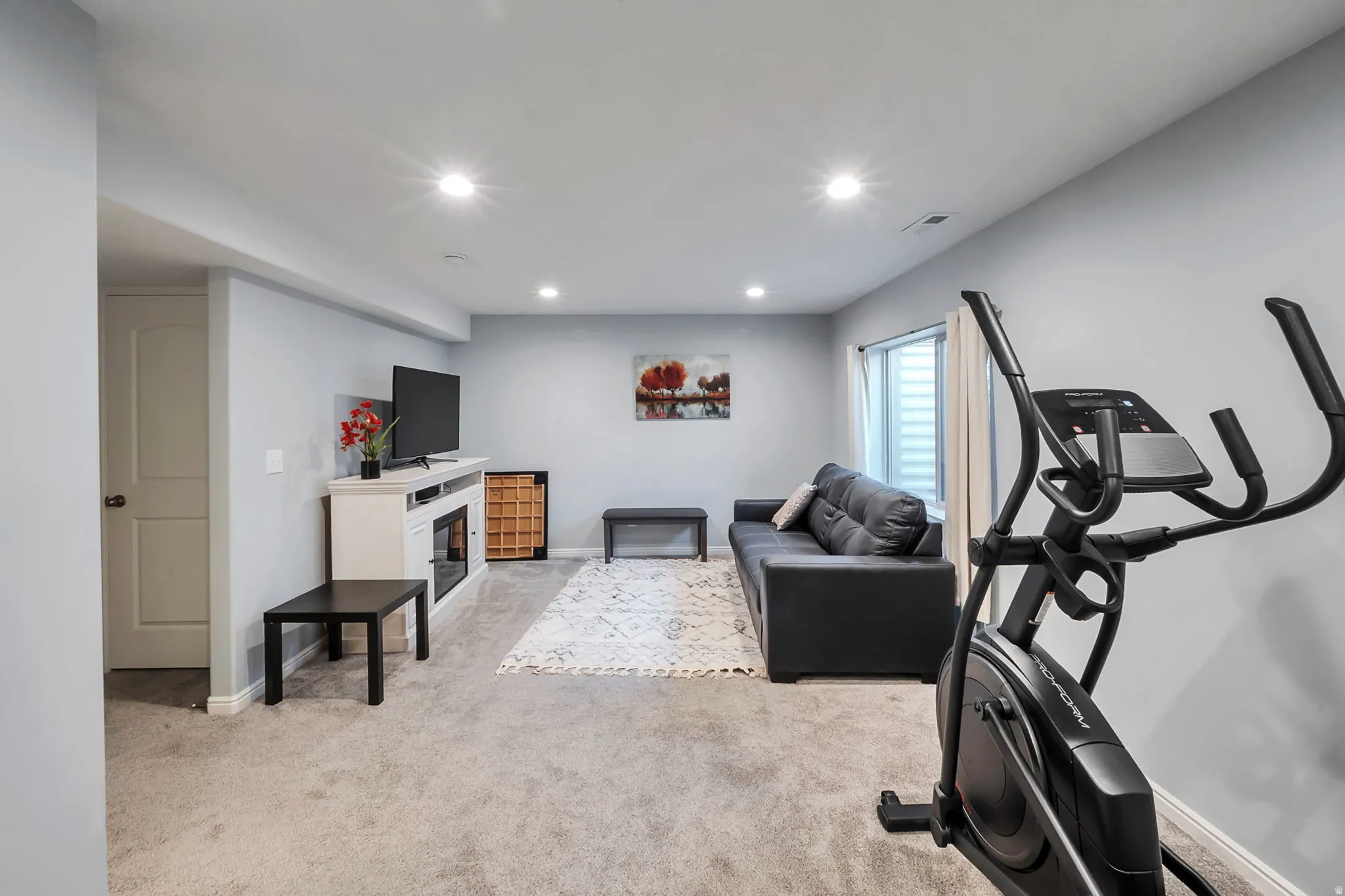 Spacious carpeted room featuring recessed lighting, a built-in electric fireplace unit, a white paneled door, and a horizontal window with blinds