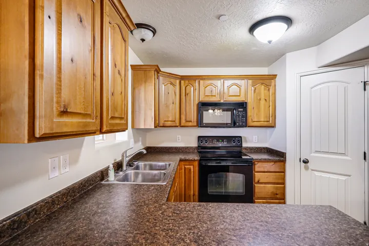 Kitchen featuring wood cabinetry, black appliances, a double basin stainless steel sink, and speckled countertops