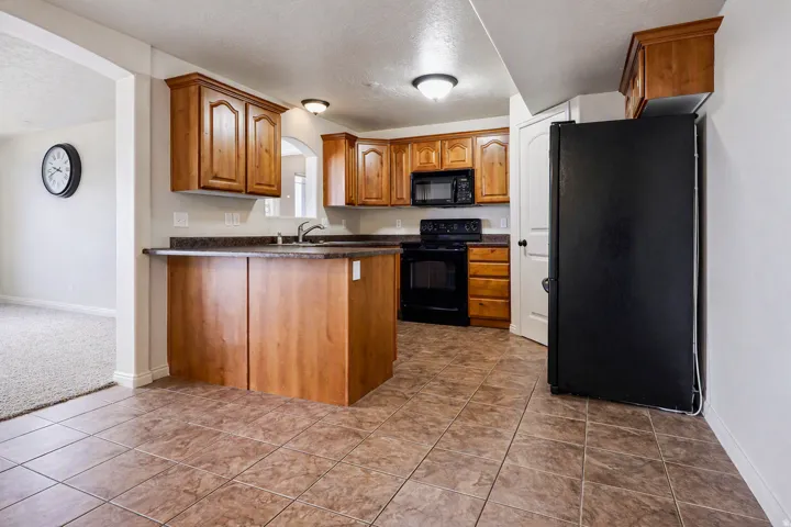 Kitchen featuring wood cabinetry, dark countertops, black appliances, and tile flooring