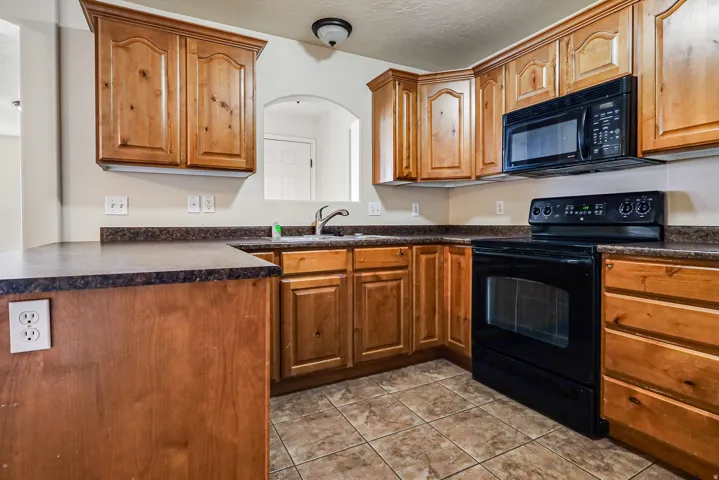 Kitchen featuring wood-finish cabinetry, dark countertops, tile flooring, and integrated black appliances including a microwave and range