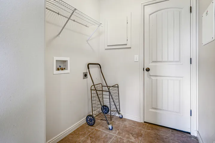 Laundry area with wire shelving, wall-mounted water hookups, and tiled flooring