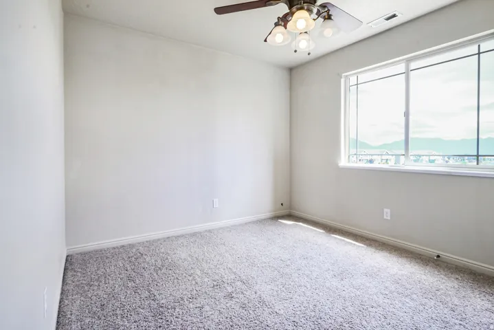 Expansive window with mountain backdrop, ceiling fan with integrated lighting, and carpeted flooring